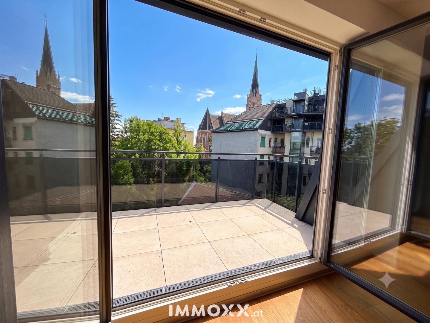 Heller Blick von innen auf die großzügige Terrasse mit Stadtpanorama und historischer Kirchenarchitektur.