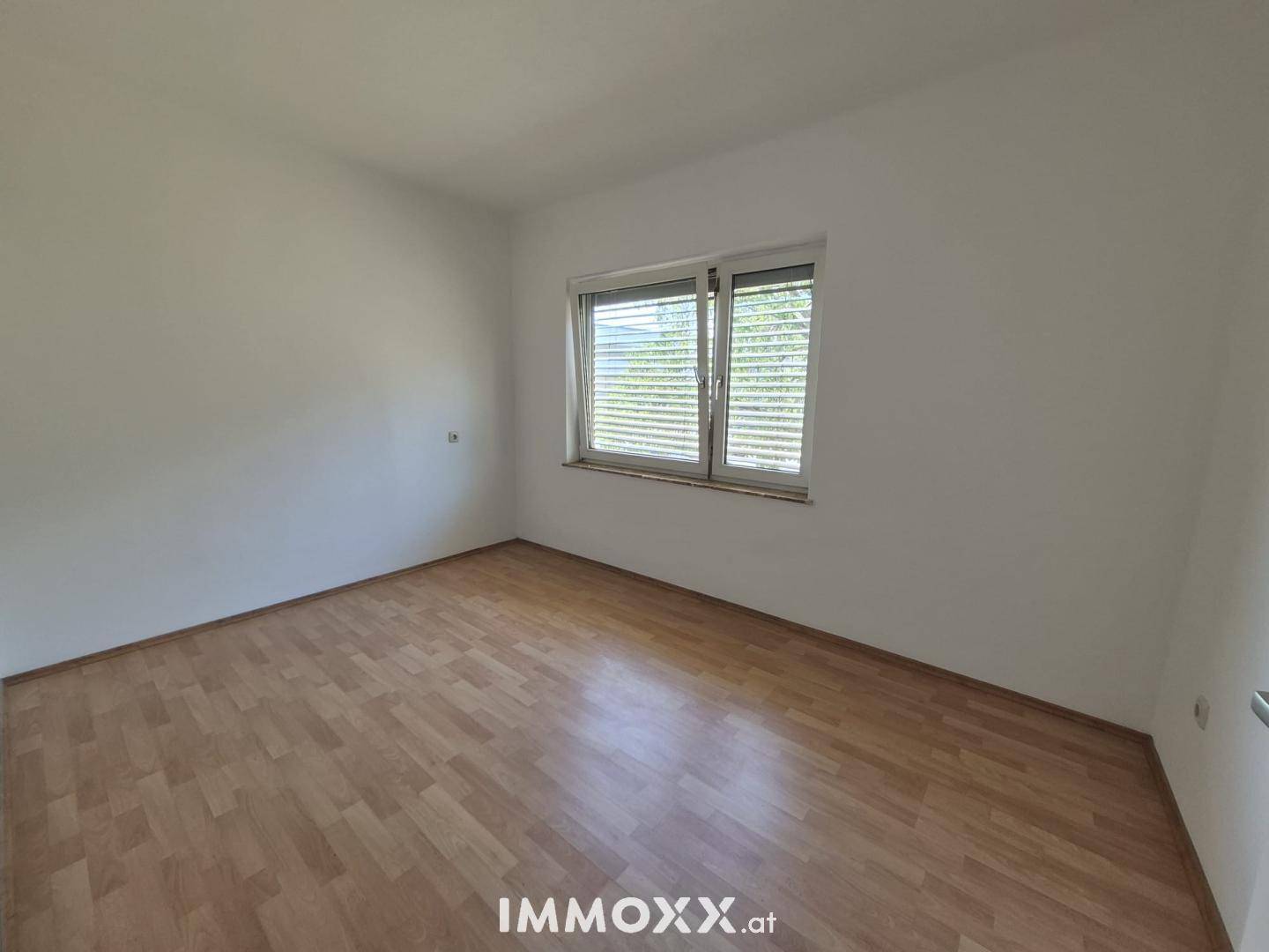 Helles Schlafzimmer mit Laminatboden und einem Fenster, das viel Tageslicht hereinlässt.