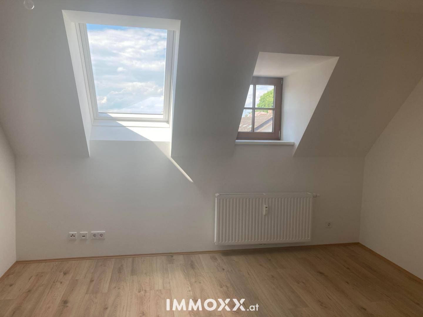 Helles Dachgeschosszimmer mit Laminatboden, Dachfenster und einem weiteren kleinen Fenster für optimale Belichtung.