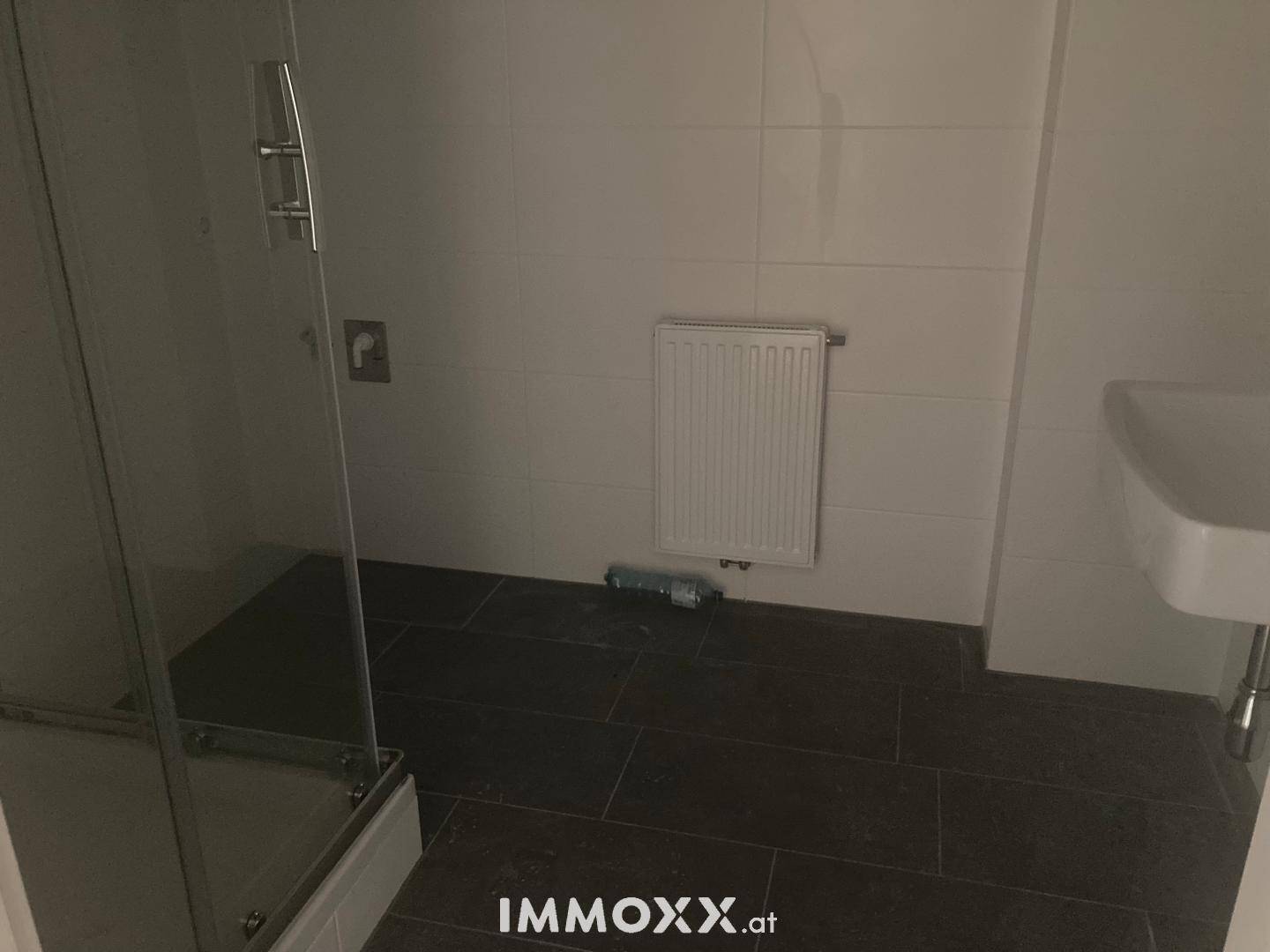 Modernes Badezimmer mit dunklen Fliesen, Duschkabine und Waschbecken, funktional und sauber gestaltet.