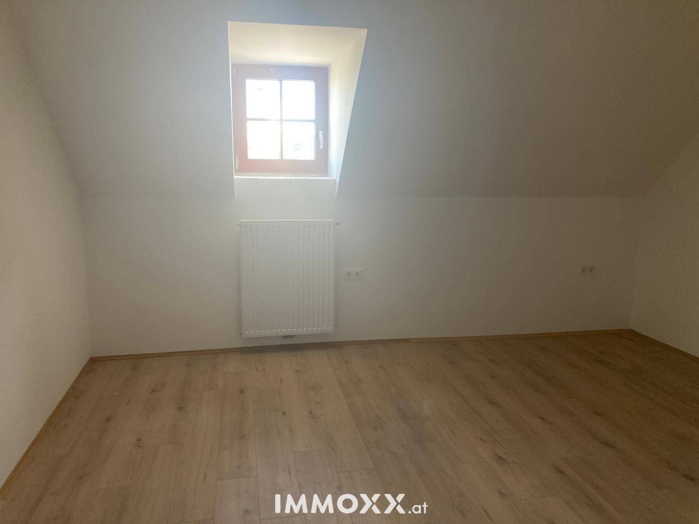 Helles Zimmer im Dachgeschoss mit Laminatboden, Heizkörper und einem kleinen Fenster, ideal als Schlaf- oder Arbeitszimmer.