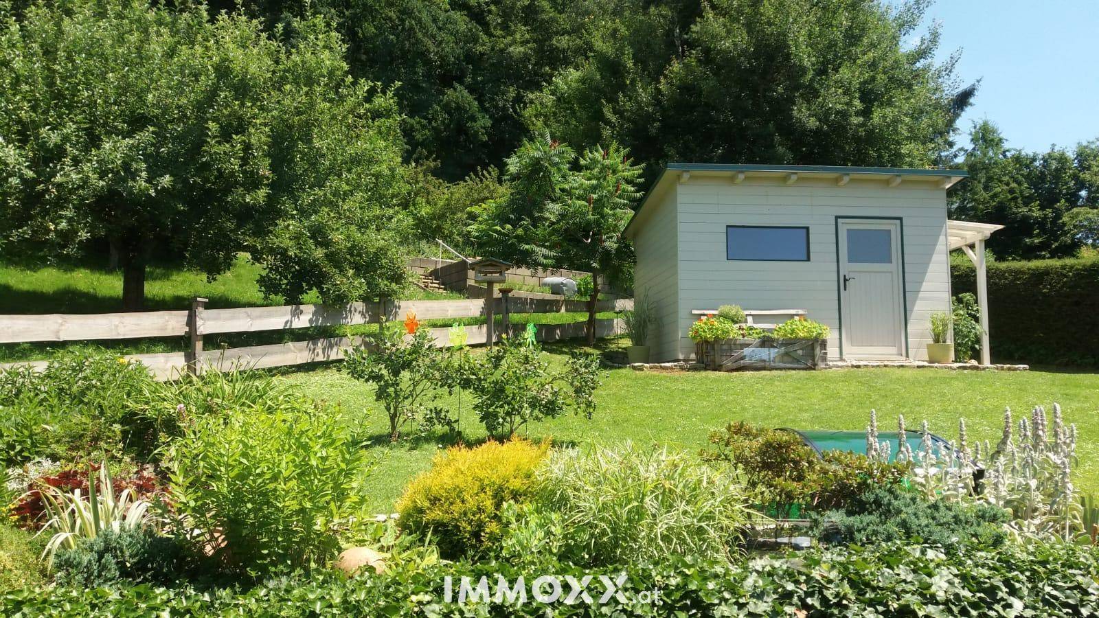 Gepflegter Gartenbereich mit Rasenfläche, Sträuchern und einem praktischen Gartenhaus im Grünen.