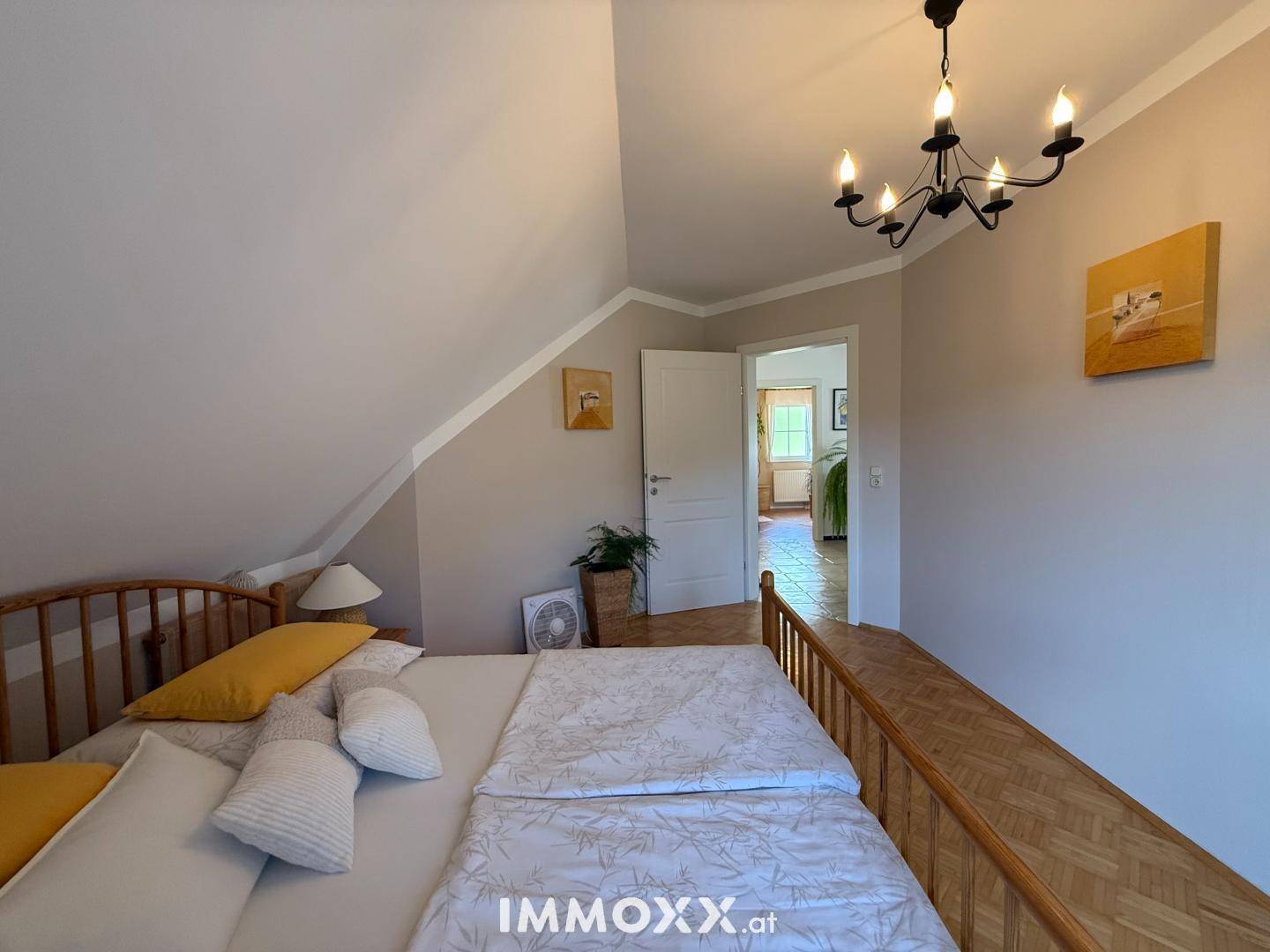 Schlafzimmer im Dachgeschoss mit schrägen Wänden, Holzbett und Parkettboden.