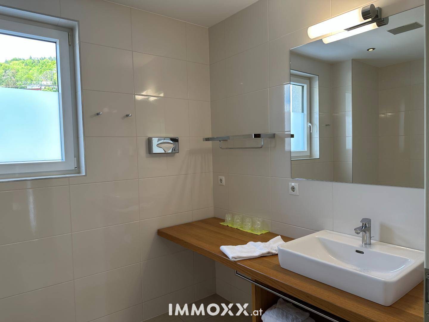 Modernes Badezimmer mit hellem Fliesenboden, Einzelwaschbecken und Fenster.