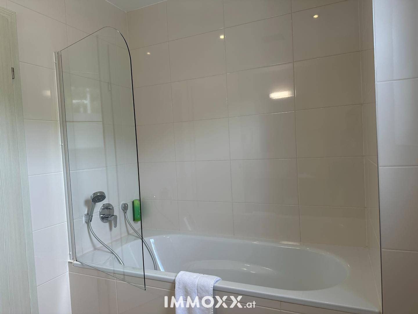 Helles Badezimmer mit Badewanne und Duschwand, komplett gefliest.