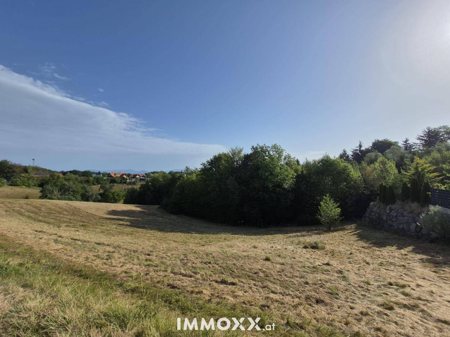 Sonnige Landschaft mit Feldern, Bäumen und Häusern in der Ferne unter blauem Himmel.