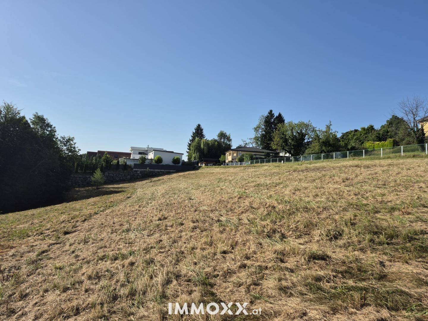 Weitläufiges, leicht abfallendes Feld mit modernen Häusern am oberen Rand und blauem Himmel.