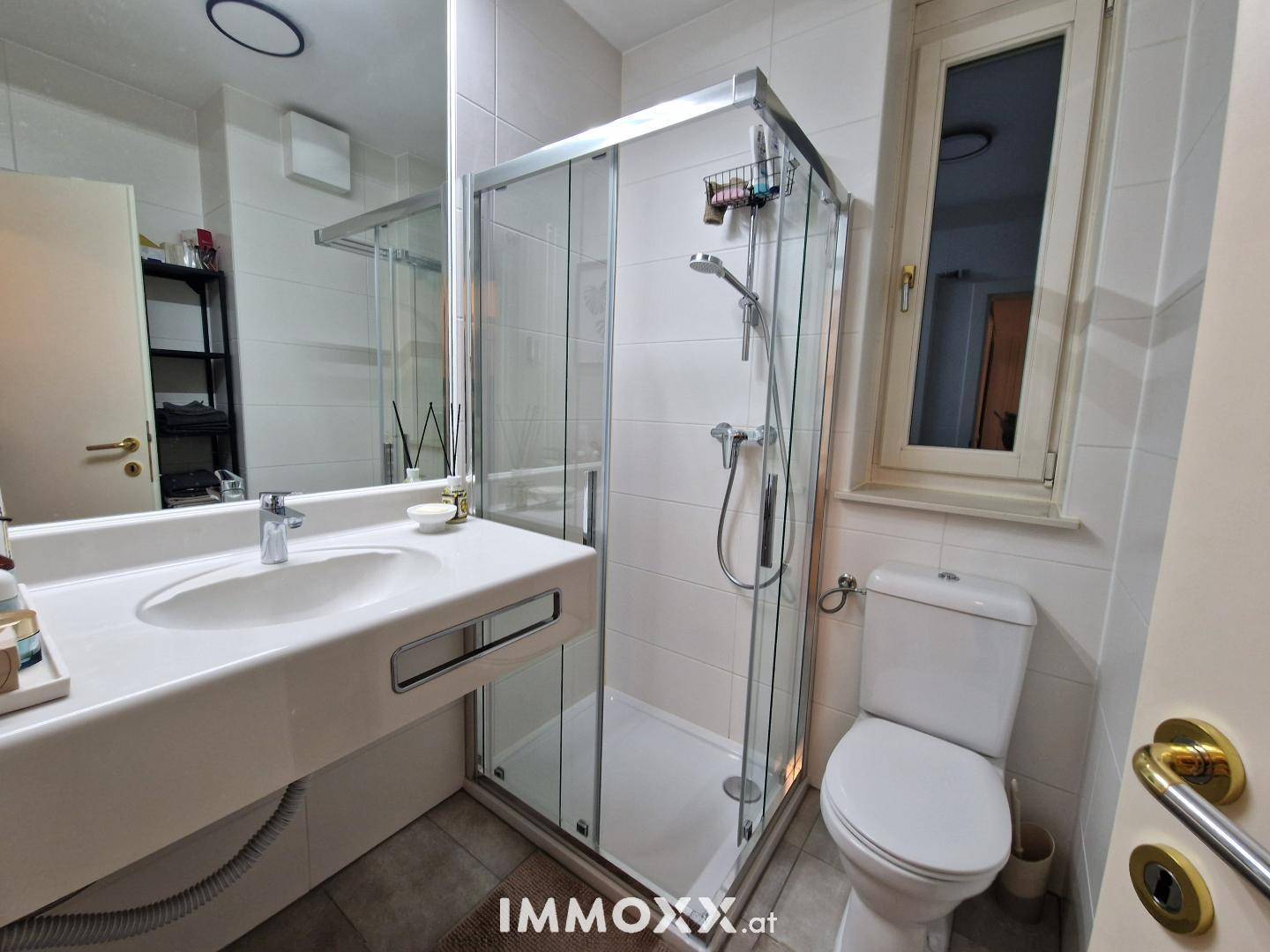 Modernes Badezimmer mit Dusche, Waschbecken, Toilette und Fenster für Tageslicht.