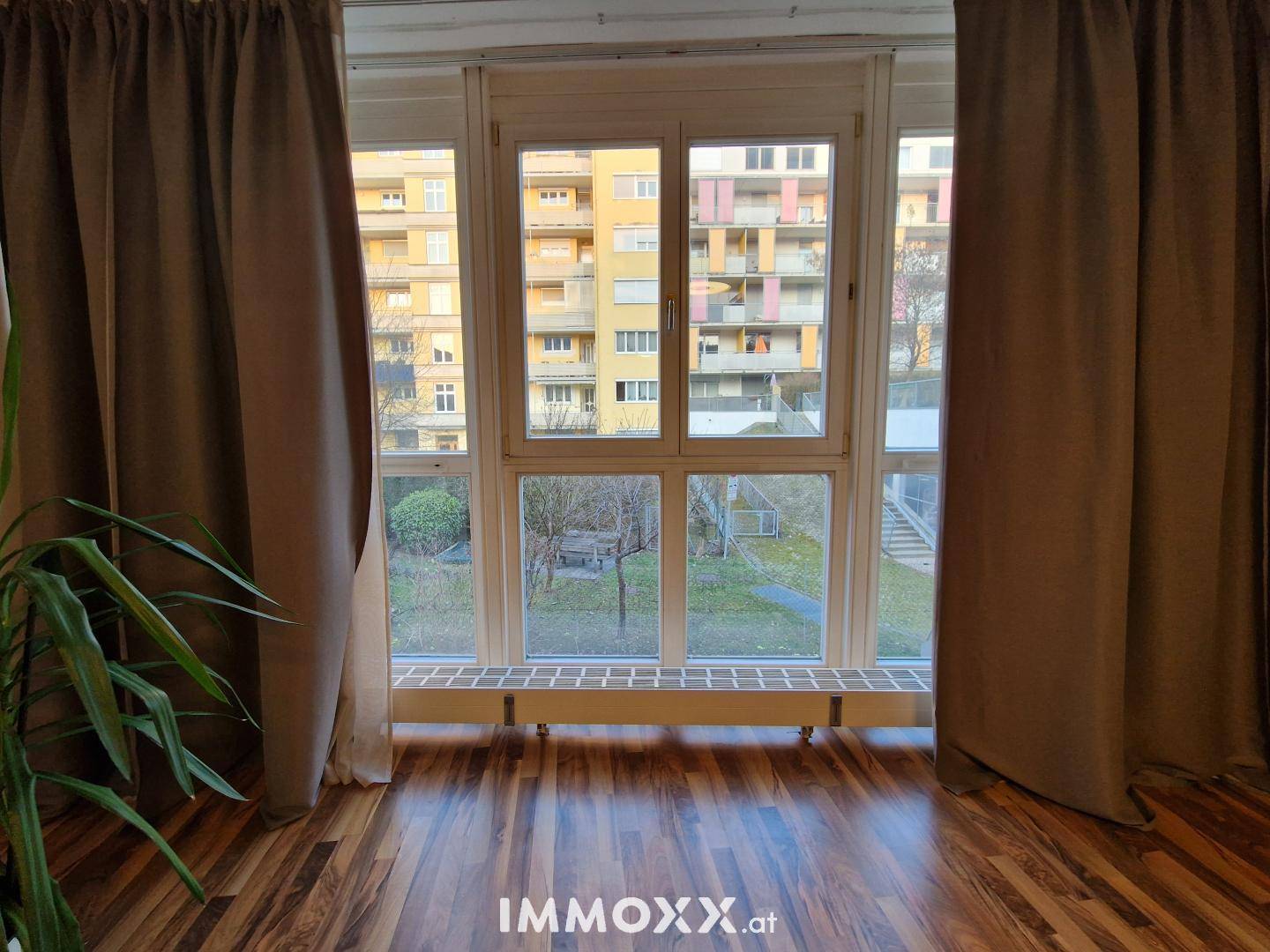 Fenster mit Blick auf den Innenhof und andere Gebäude, umgeben von Vorhängen.