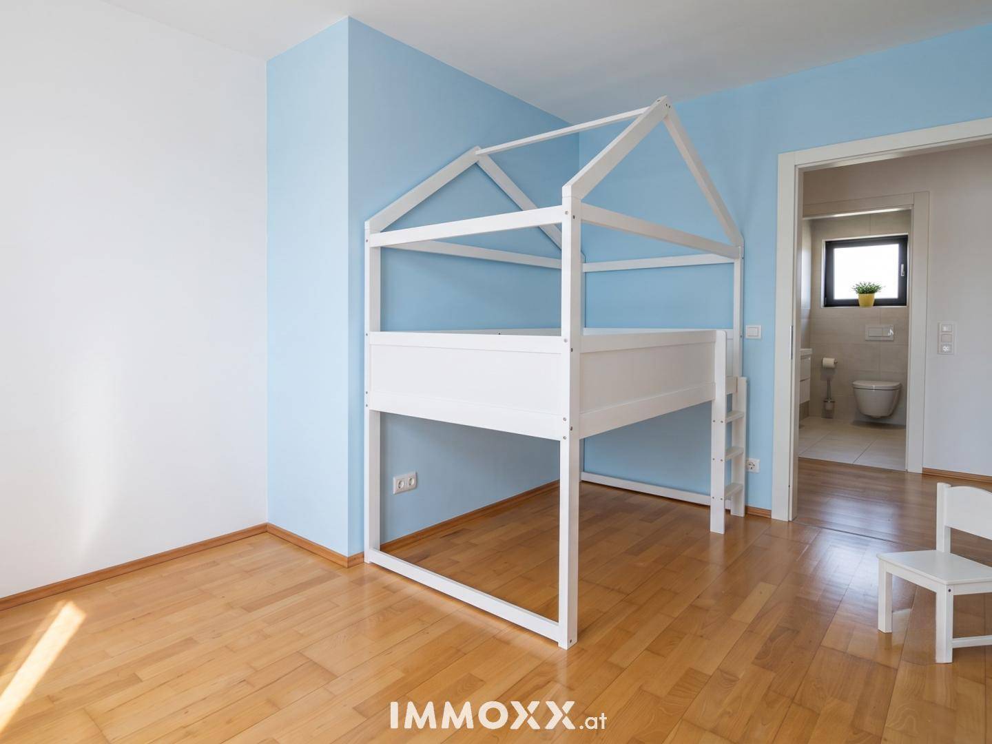 Kinderzimmer mit blau gestrichener Wand, Holzbettgestell und Zugang zum Badezimmer.