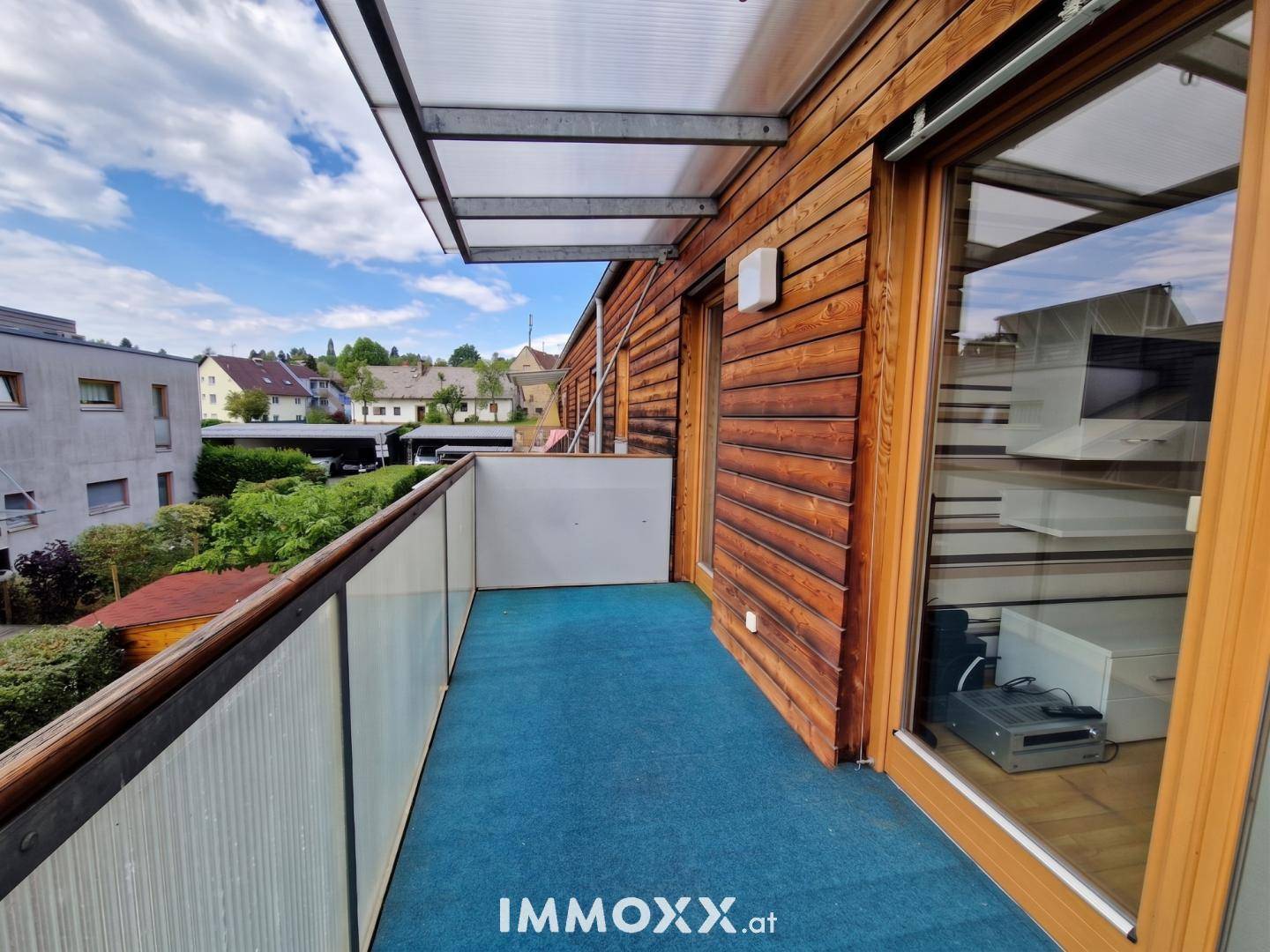 Geräumiger Balkon mit Teppichboden, Glasgeländer und weitem Blick über die Nachbarschaft.