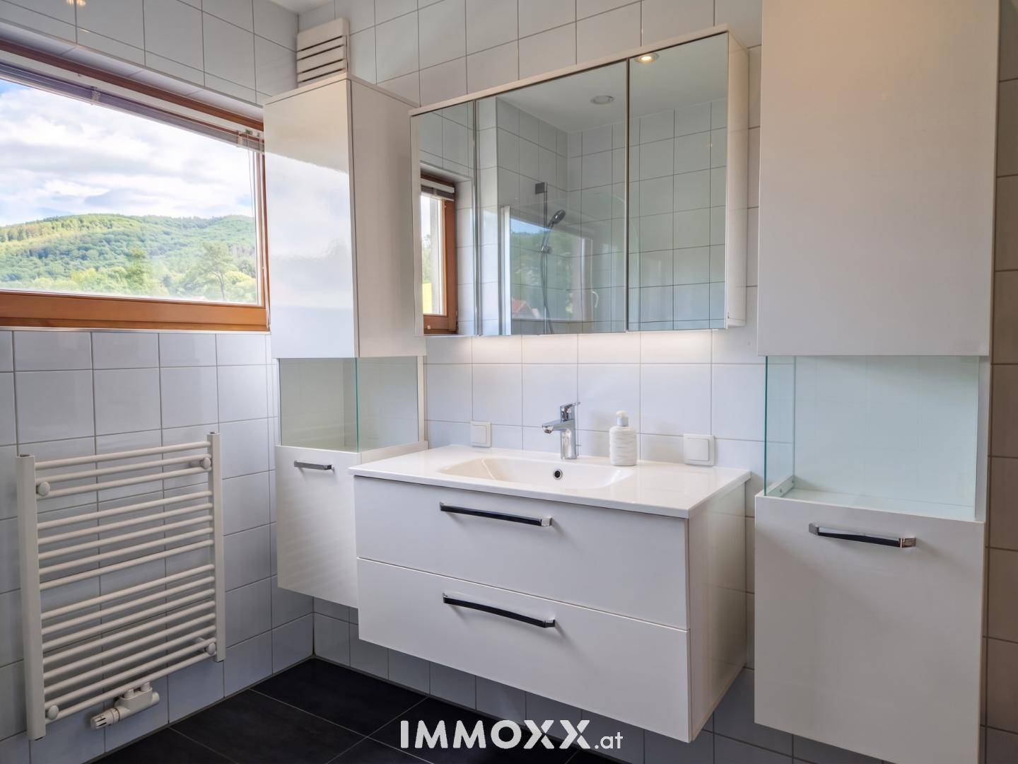 Modernes Badezimmer mit Waschtisch, Spiegelschrank, Fenster und Handtuchheizkörper.