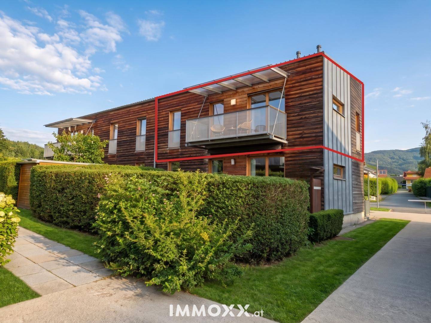 Moderne Reihenhausfassade mit Holzverkleidung, Balkon und gepflegter Hecke.