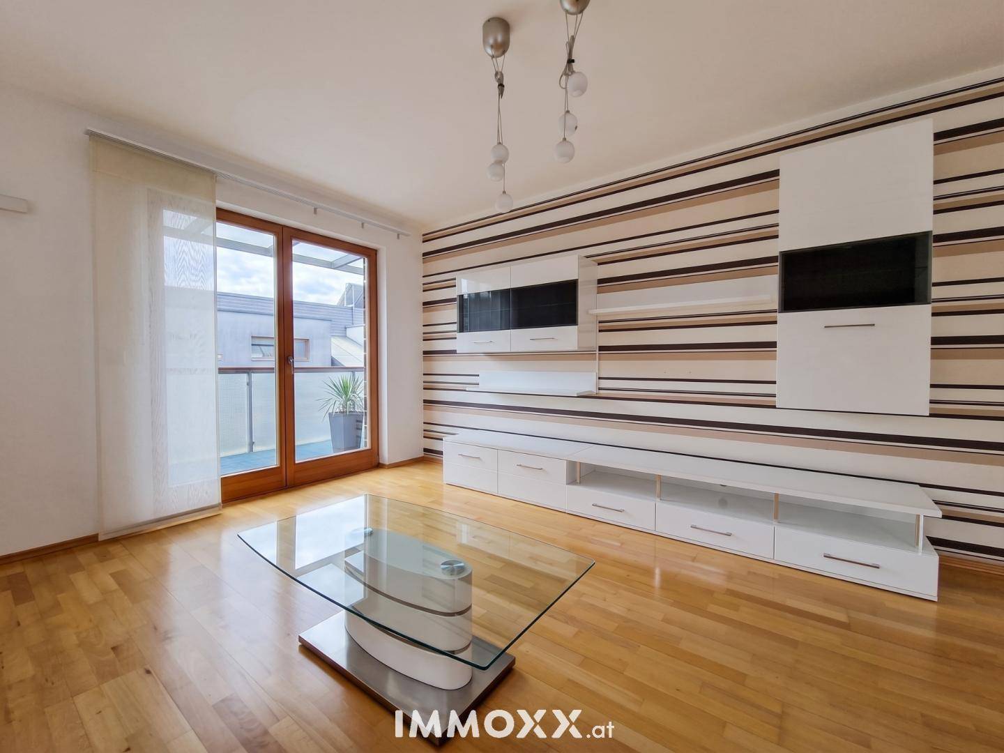 Helles Wohnzimmer mit Parkettboden, moderner Wohnwand und Zugang zum Balkon.