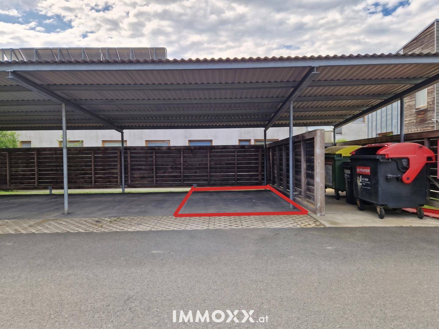 Überdachter Parkplatz mit Carport-Struktur und Mülltonnenbereich.