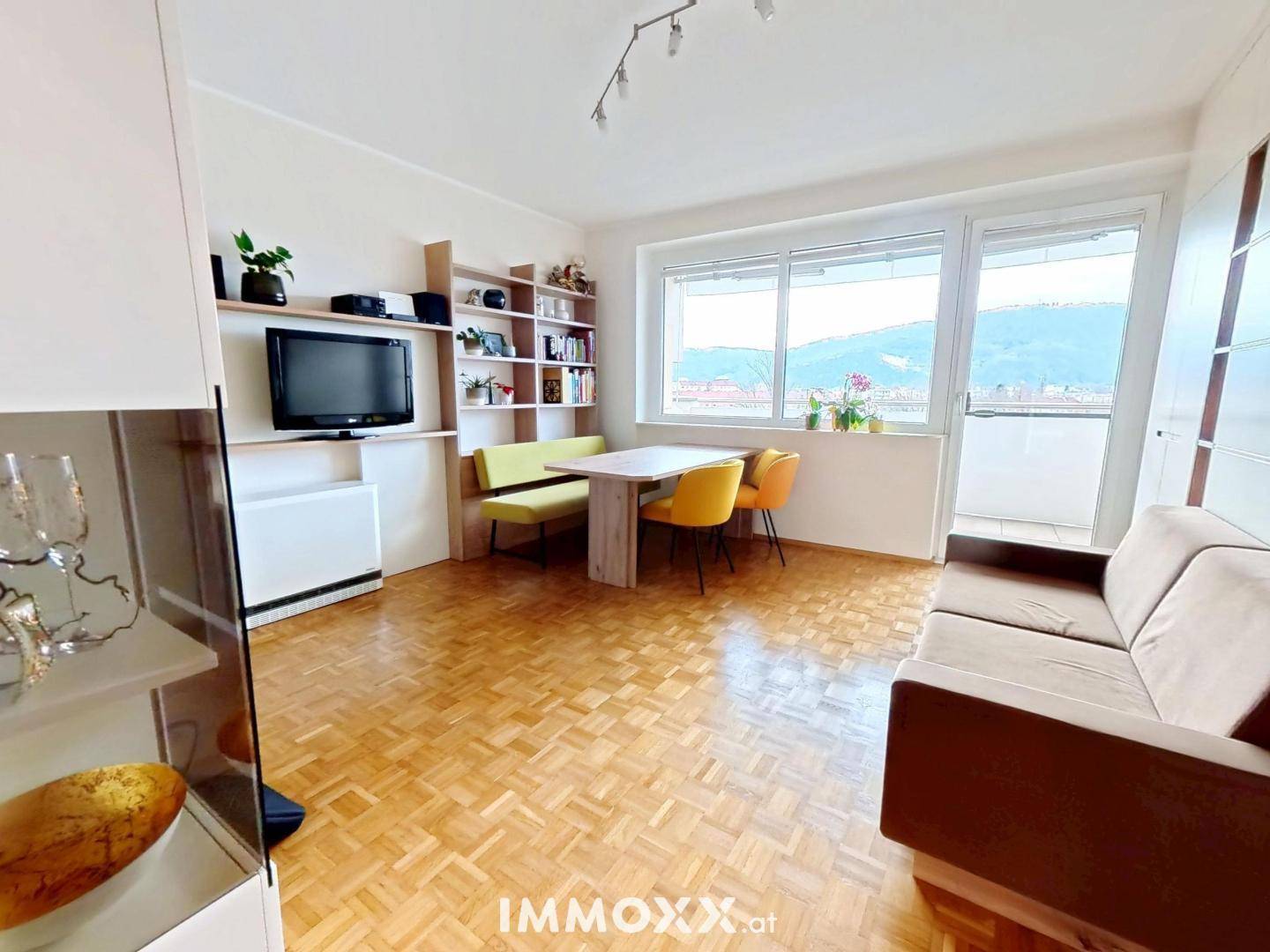 Wohn-Essbereich mit Sofa, Esstisch, TV-Möbel und großem Fenster, das viel Licht hereinlässt.