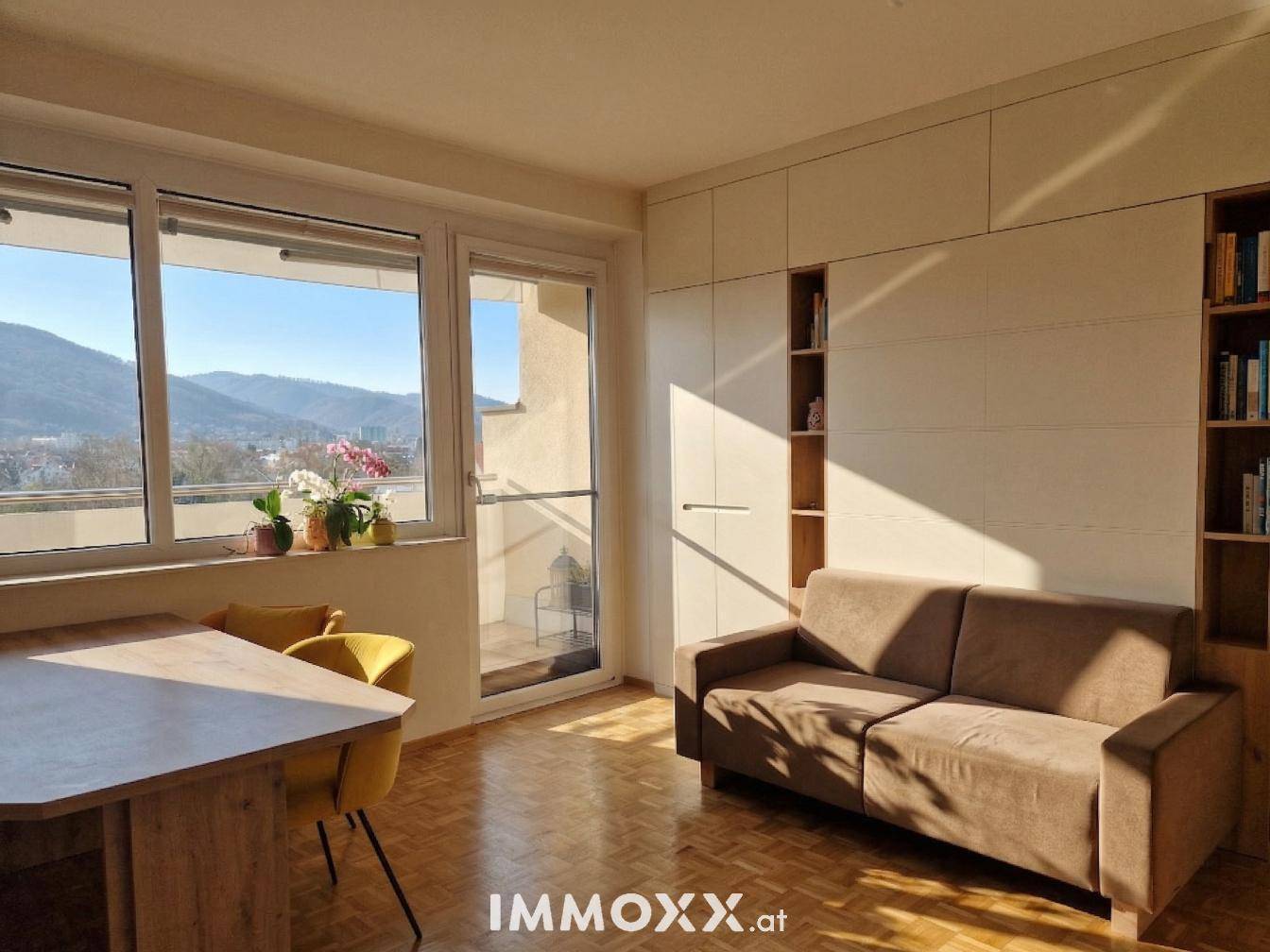 Heller Wohn-Essbereich mit Parkettboden, Sofa, Esstisch und Zugang zu einem Balkon mit Bergblick.
