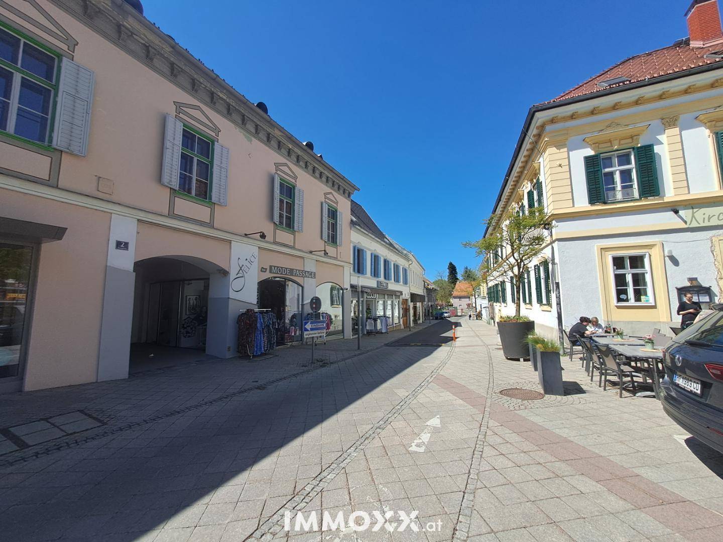 Eine charmante Gasse mit historischen Gebäuden, Außengastronomie und Fußgängern.