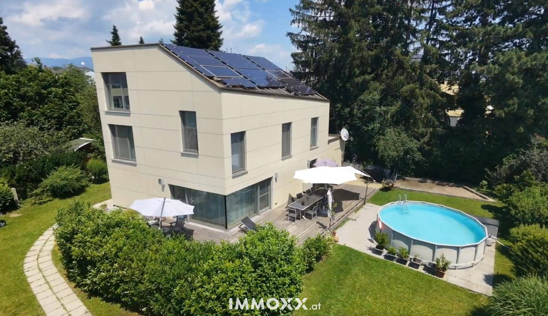 Modernes Haus mit Solaranlage, großem Garten, Holzterrasse und Aufstellpool umgeben von Bäumen.