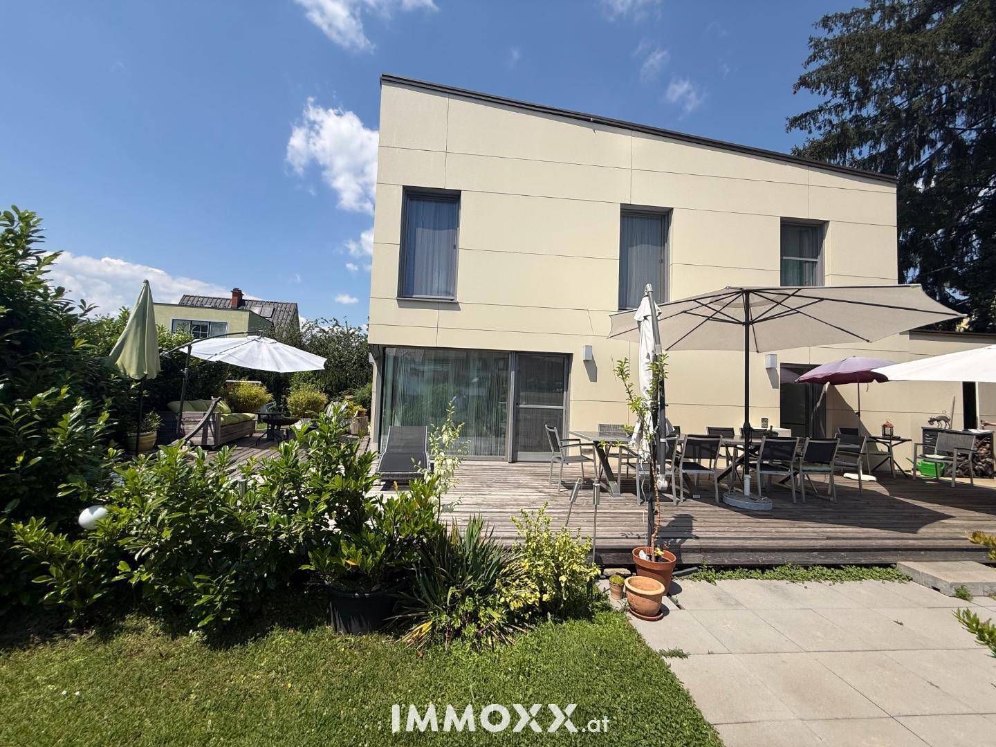 Große Holzterrasse mit Essbereich und Sonnenschirmen, umgeben von einem gepflegten Garten.