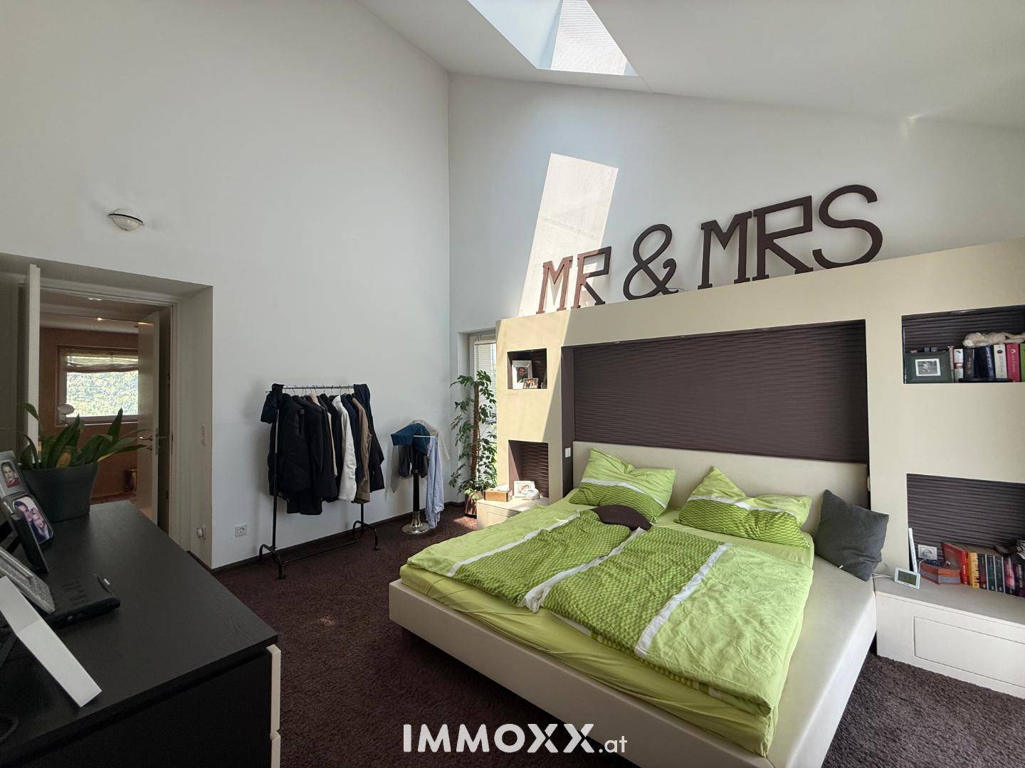 Modernes Schlafzimmer mit Bett, großem Spiegel und viel natürlichem Licht durch das Oberlicht.