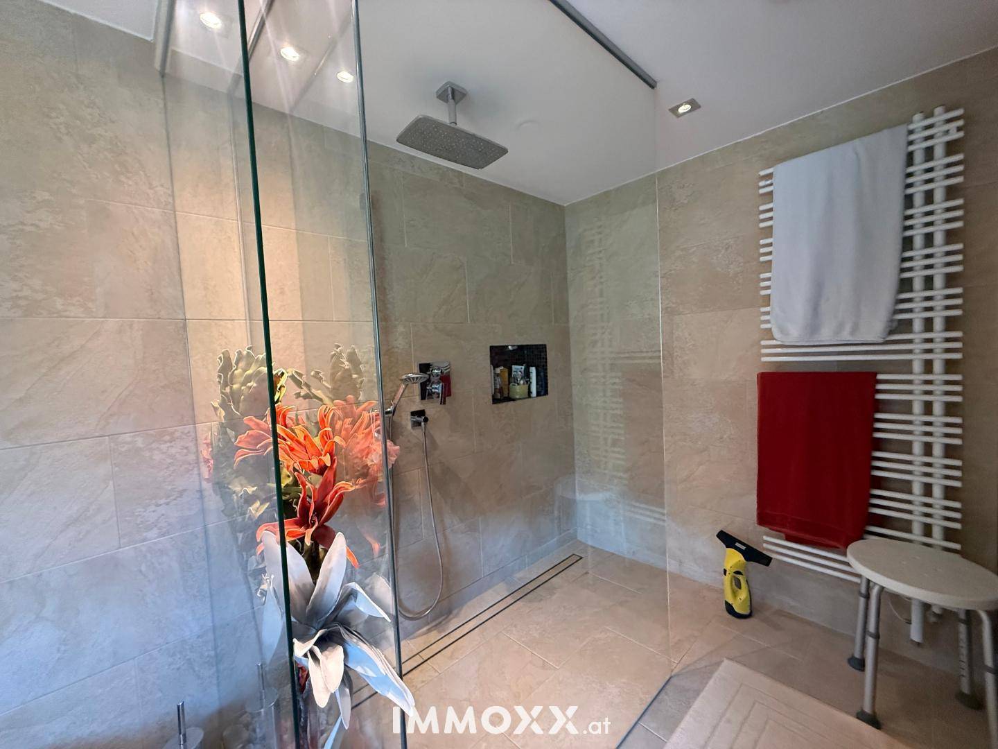 Moderne begehbare Dusche mit Regenduschkopf, Glasabtrennung und beheiztem Handtuchhalter.