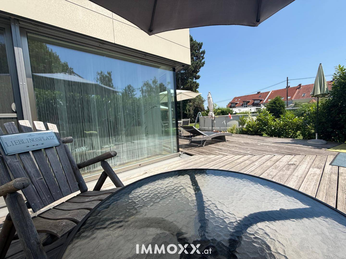 Gemütlicher Sitzbereich auf der Holzterrasse mit Blick auf den Garten und große Glasfronten.