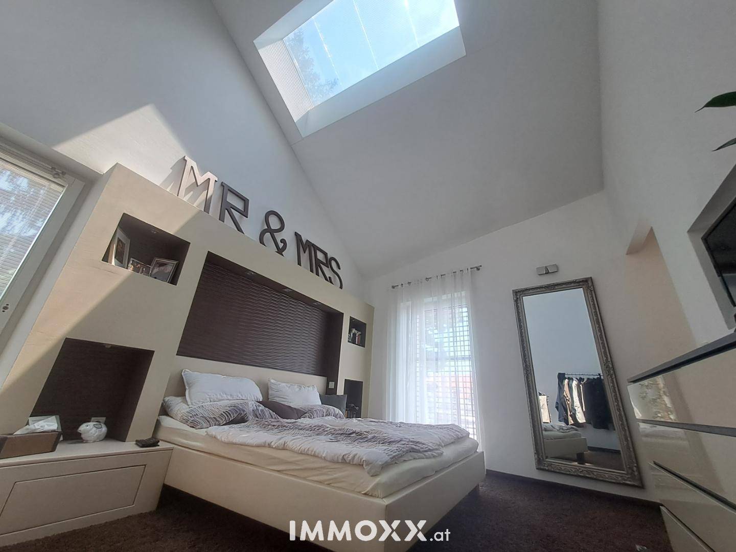 Schlafzimmer mit hohem Dach, Oberlicht und einem großen Bett, das zum Entspannen einlädt.