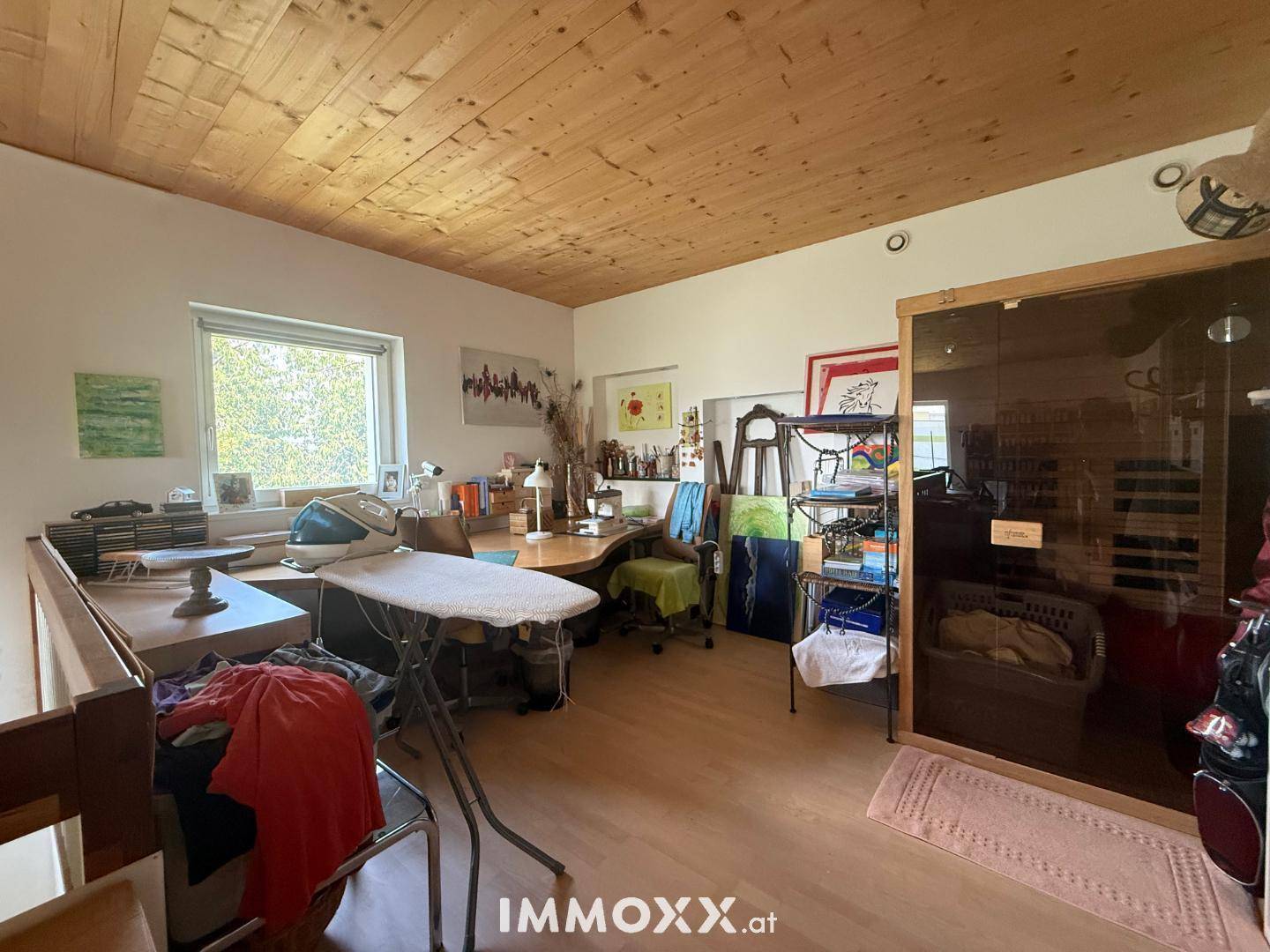 Vielseitiger Raum mit Holzboden, Schreibtischbereich, Fenster und integrierter Sauna.
