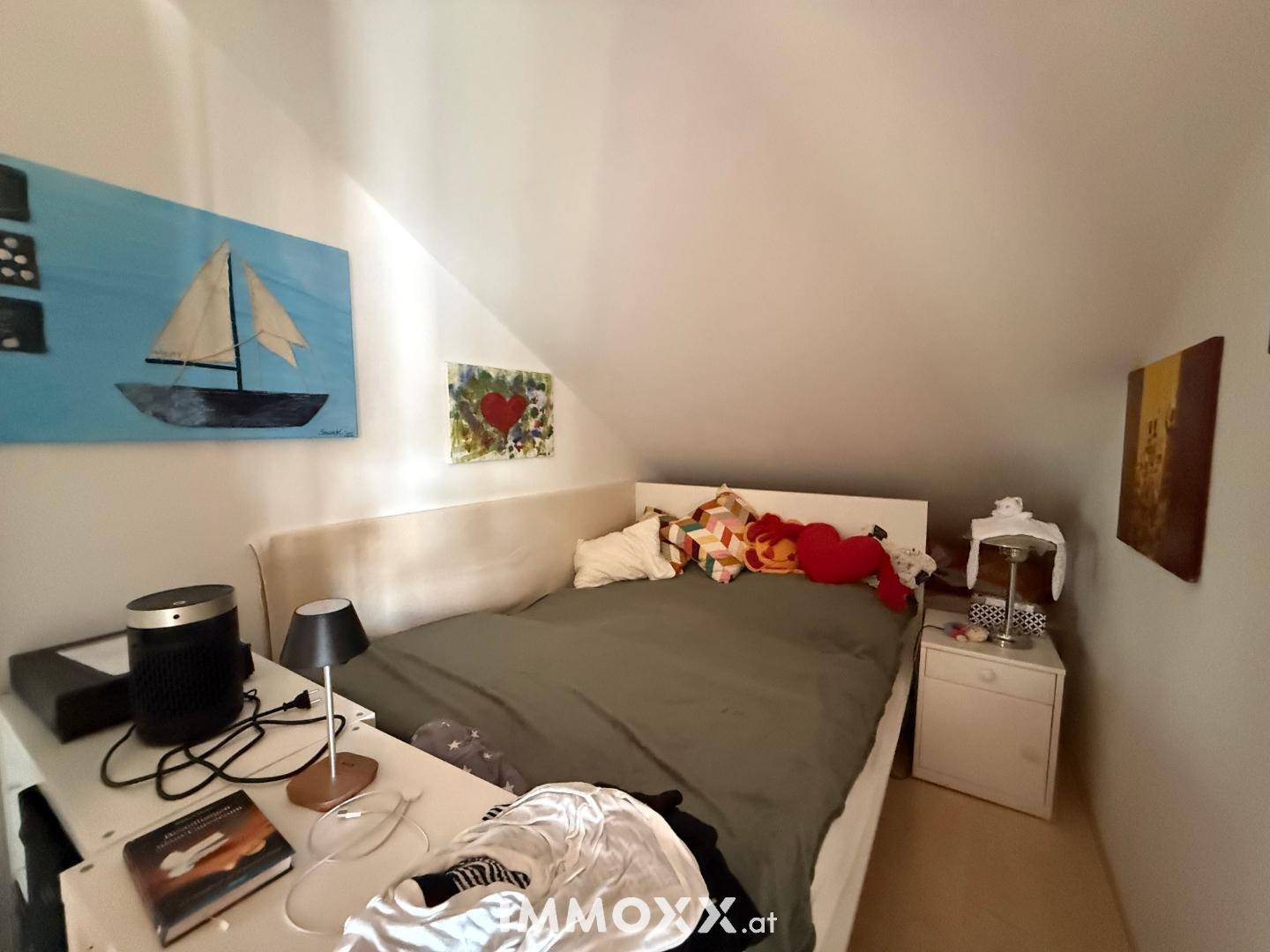 Schlafzimmer mit gemütlichem Bett, Nachttisch und schräger Decke unter dem Dach.