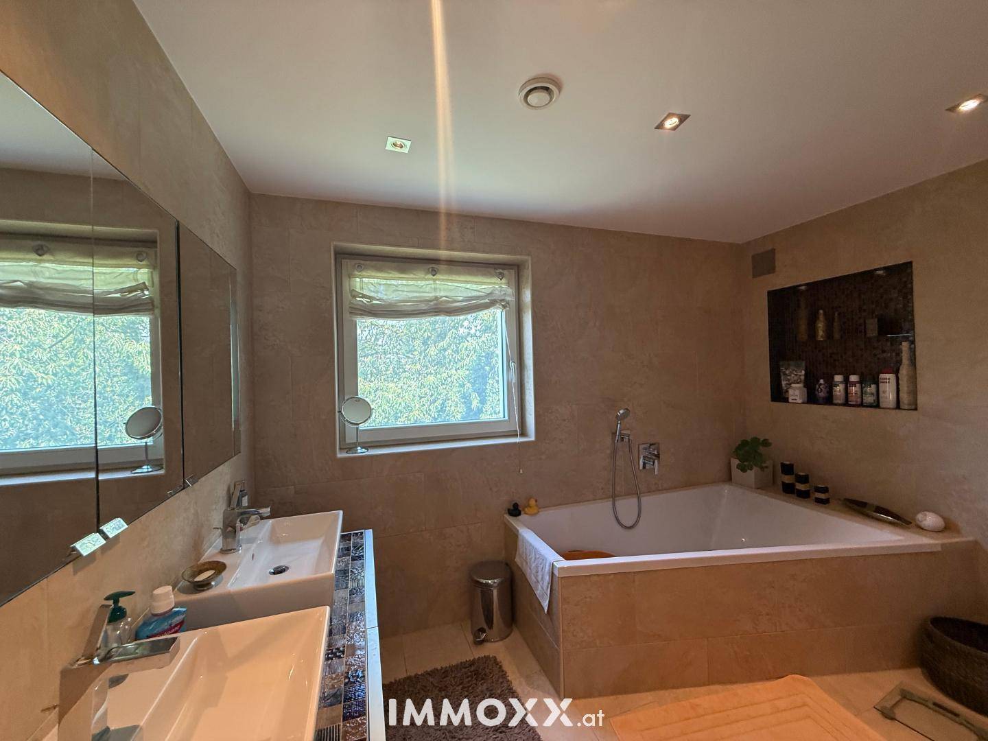 Geräumiges Badezimmer mit Doppelwaschbecken, Badewanne und Fenster mit Blick ins Grüne.
