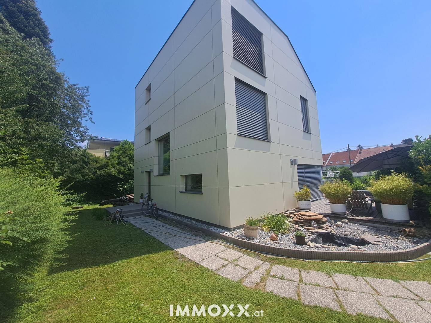 Seitenansicht des modernen Hauses mit gepflegtem Garten, Rasenfläche und einem Steinweg.