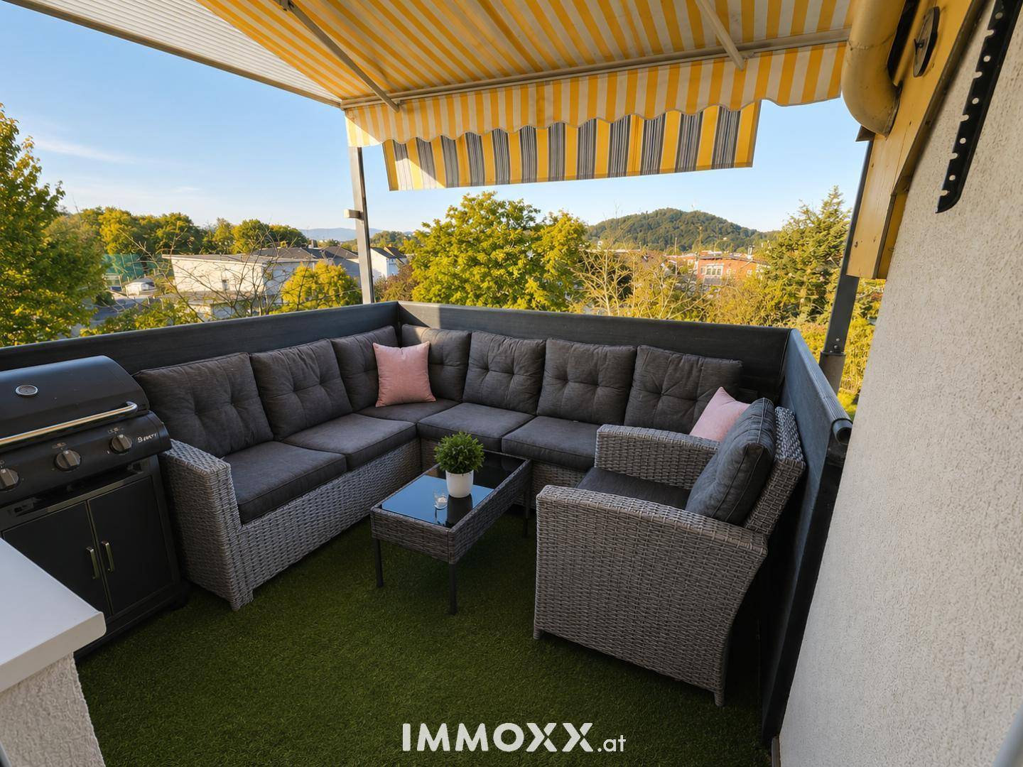 Geräumiger Balkon mit gemütlicher Lounge-Sitzgruppe, Grill und Markise, ideal für entspannte Stunden im Freien mit Blick ins Grüne.