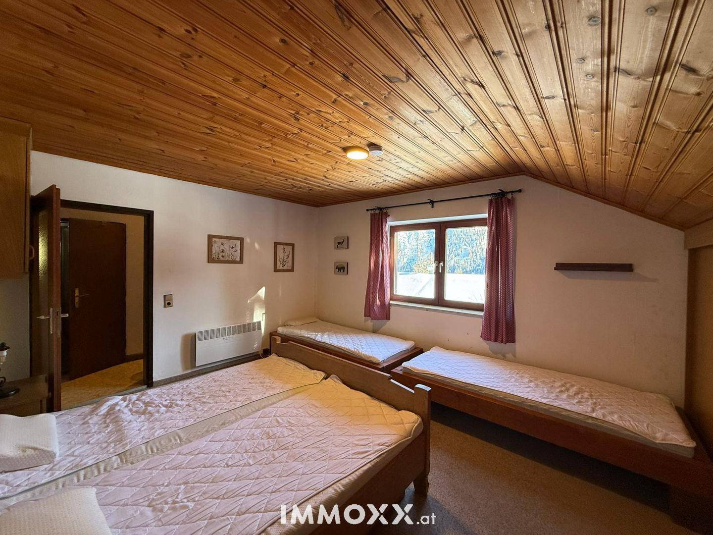 Schlafzimmer im Dachgeschoss mit Holzdecke, mehreren Betten und Blick ins Grüne.