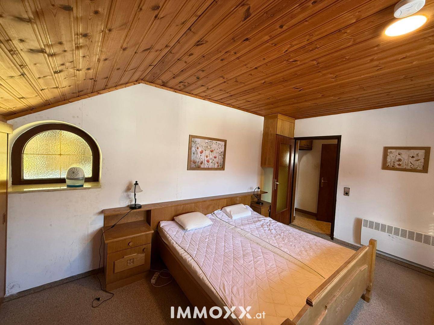 Helles Schlafzimmer mit Doppelbett, Holzdecke und einem Fenster mit Blick ins Grüne.