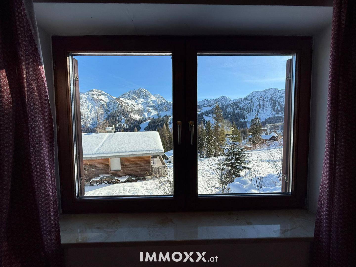 Malerischer Ausblick aus dem Fenster auf die verschneite Berglandschaft und umliegende Hütten.