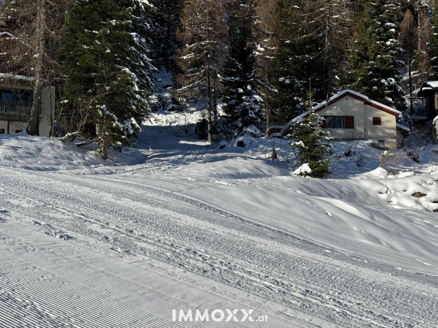 Blick auf das Anwesen von der präparierten Skipiste, umgeben von verschneiten Bäumen und Bergen.
