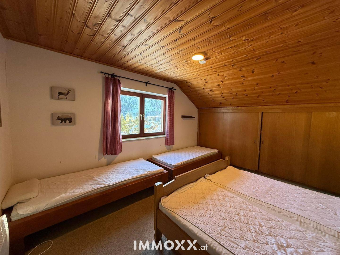 Helles Schlafzimmer im Dachgeschoss mit Holzdecke, drei Einzelbetten und Einbauschränken.