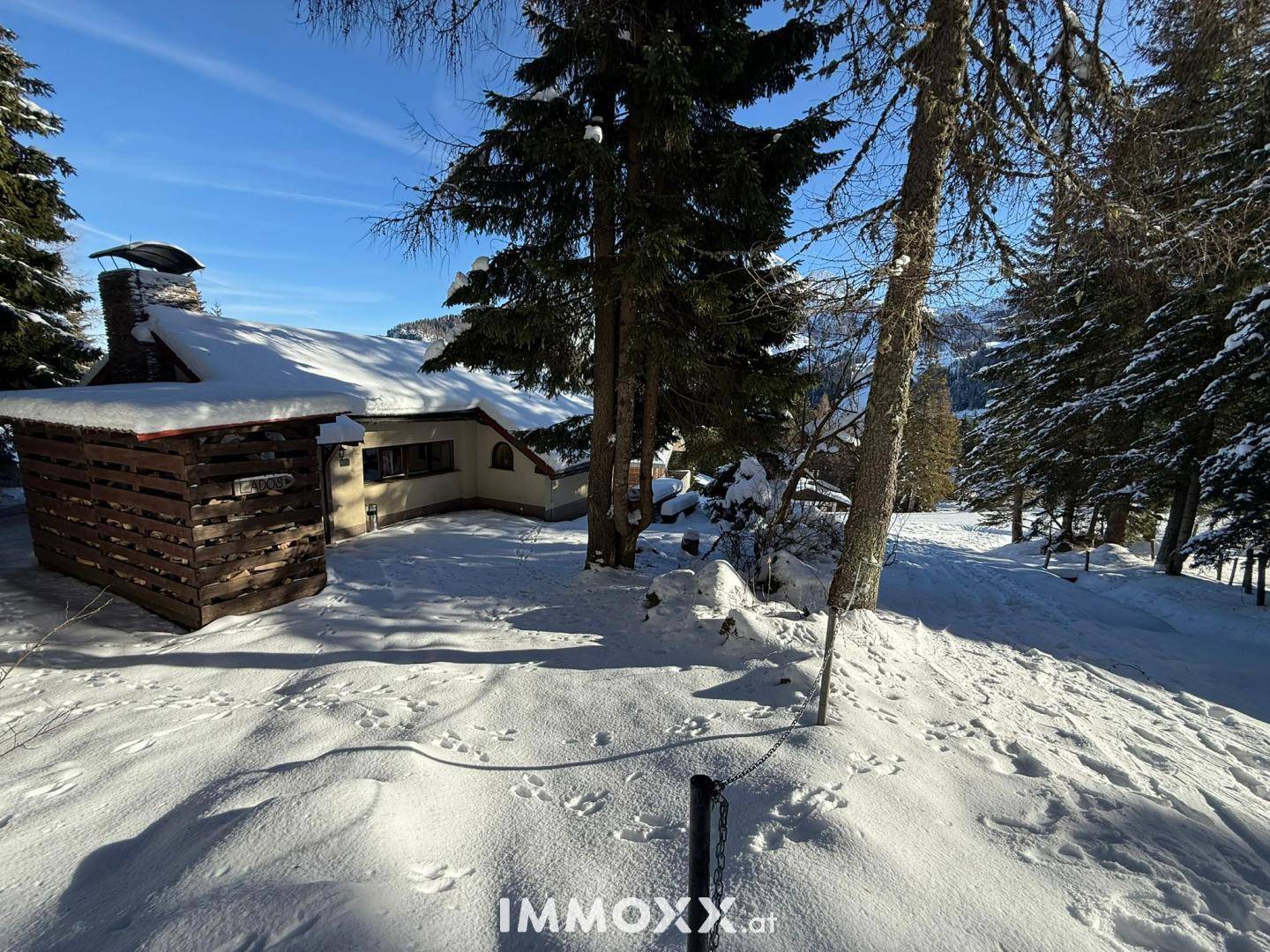 Außenansicht des Hauses im Winter mit verschneitem Dach und einem Holzschuppen im Vordergrund.
