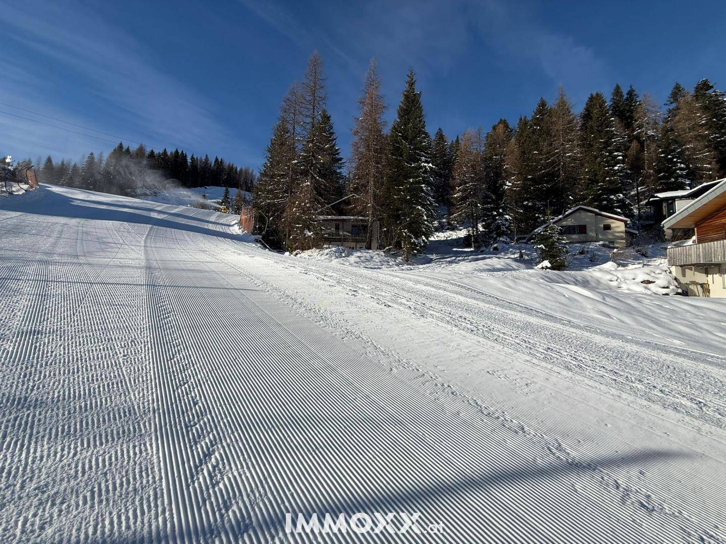 Blick auf das Anwesen von der präparierten Skipiste, umgeben von verschneiten Bäumen und Bergen.
