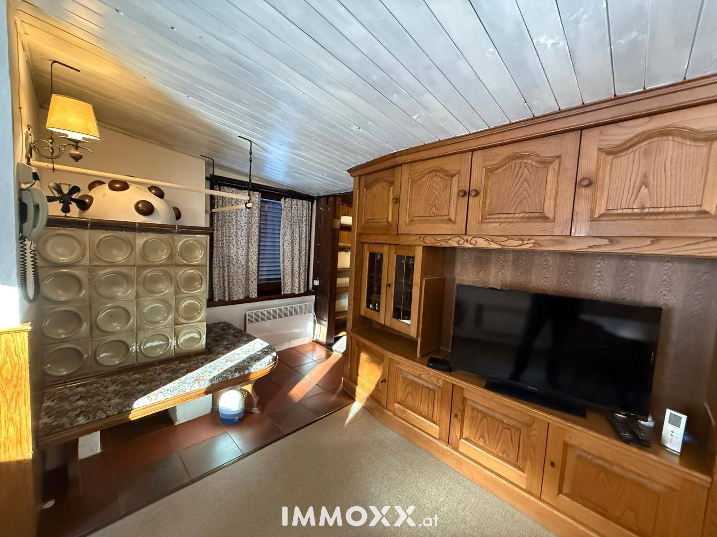 Gemütliches Wohnzimmer im alpinen Stil mit Kachelofen, Holzmöbeln und Fernseher.