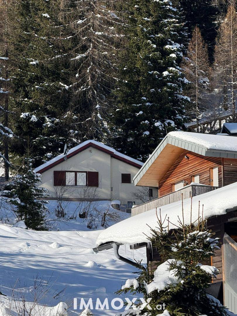 Winterliche Ansicht des Hauses mit verschneitem Dach und angrenzendem Holzhaus in den Bergen.