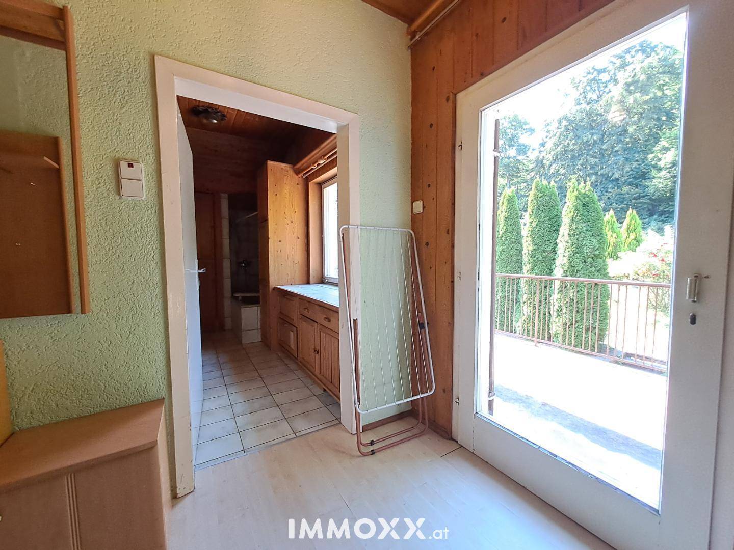 Heller Flur mit Zugang zu einem Badezimmer und einem Balkon mit Blick ins Grüne.