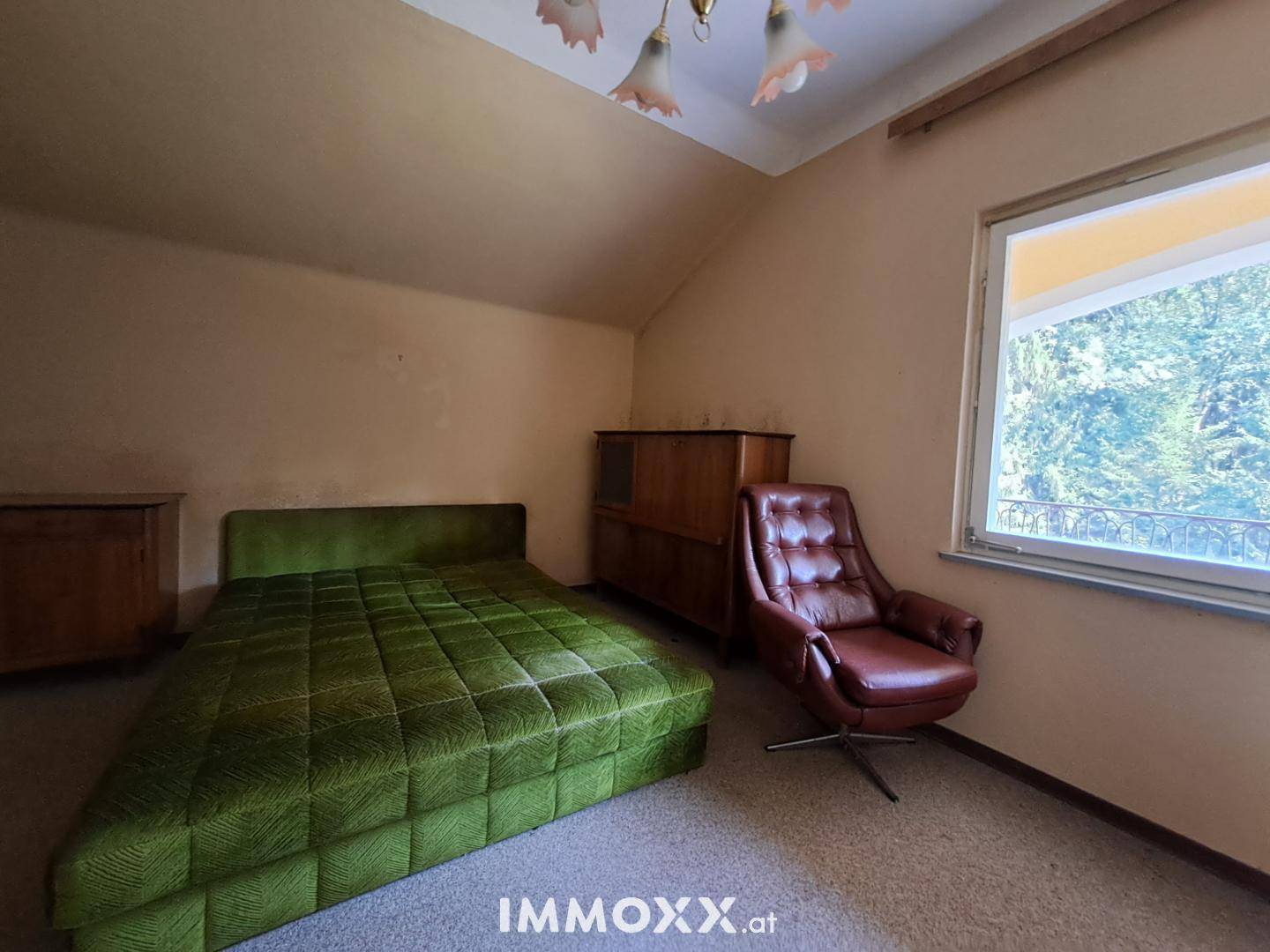 Gemütliches Schlafzimmer mit grünem Bett, Ledersessel und Blick ins Grüne.
