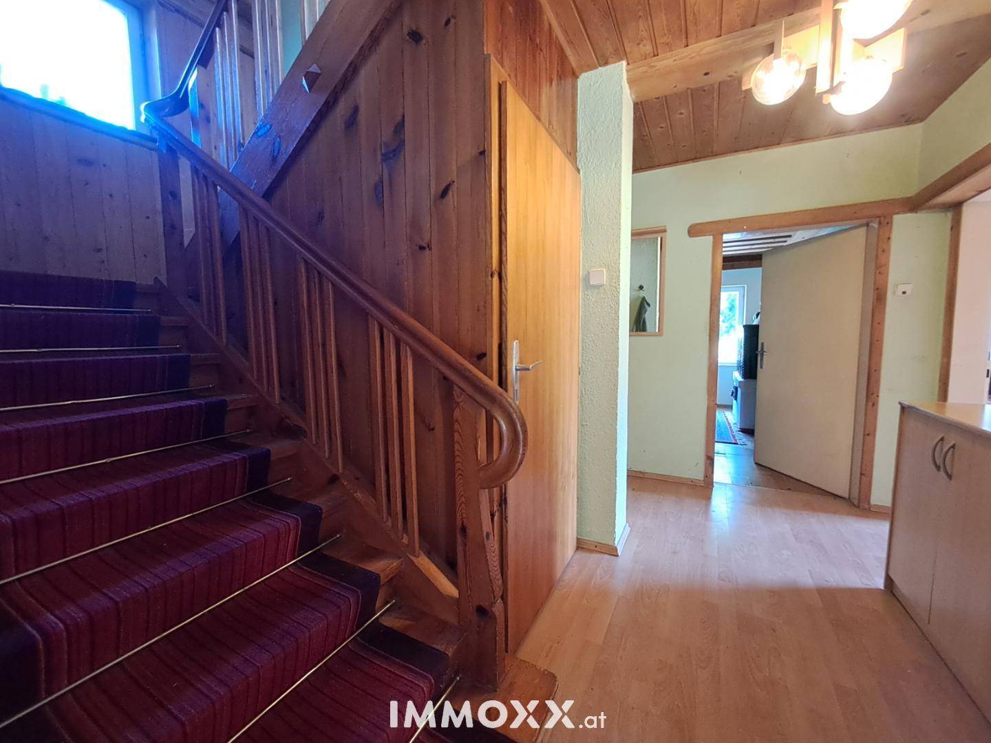 Gemütlicher Flur mit Holztreppe, Teppichboden und Holzvertäfelung an Wänden und Decke.