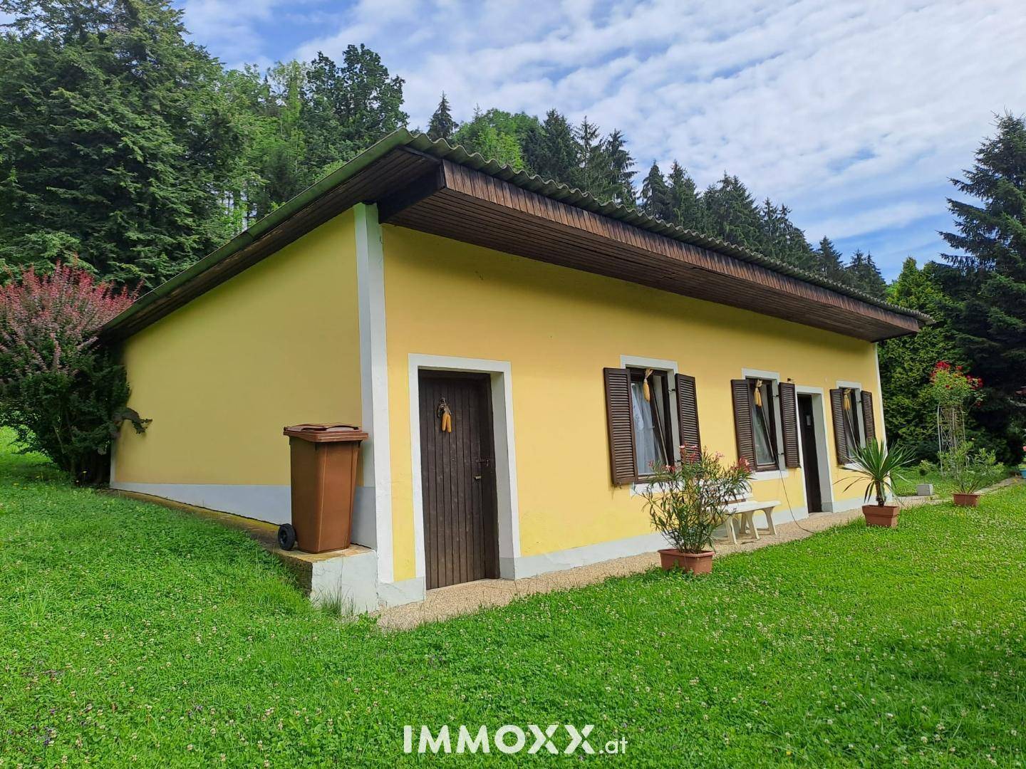 Seitenansicht des gelben Hauses mit braunen Fensterläden und einem großen Rasenbereich.