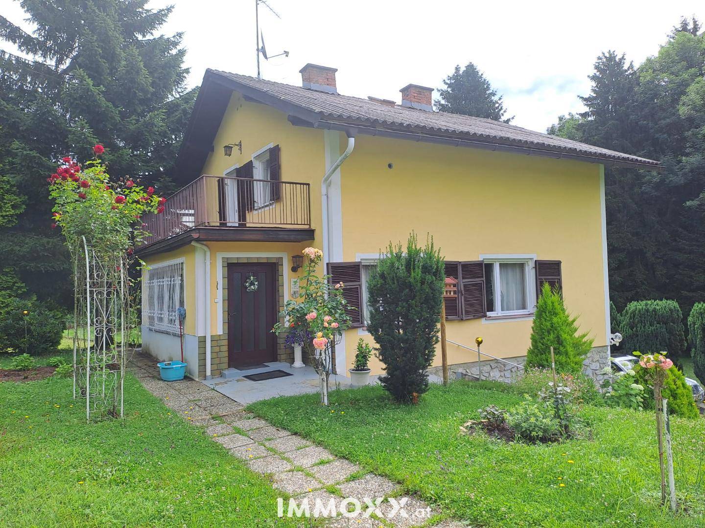 Charmantes gelbes Haus mit Balkon und traditionellen Fensterläden, eingebettet in eine grüne Landschaft.