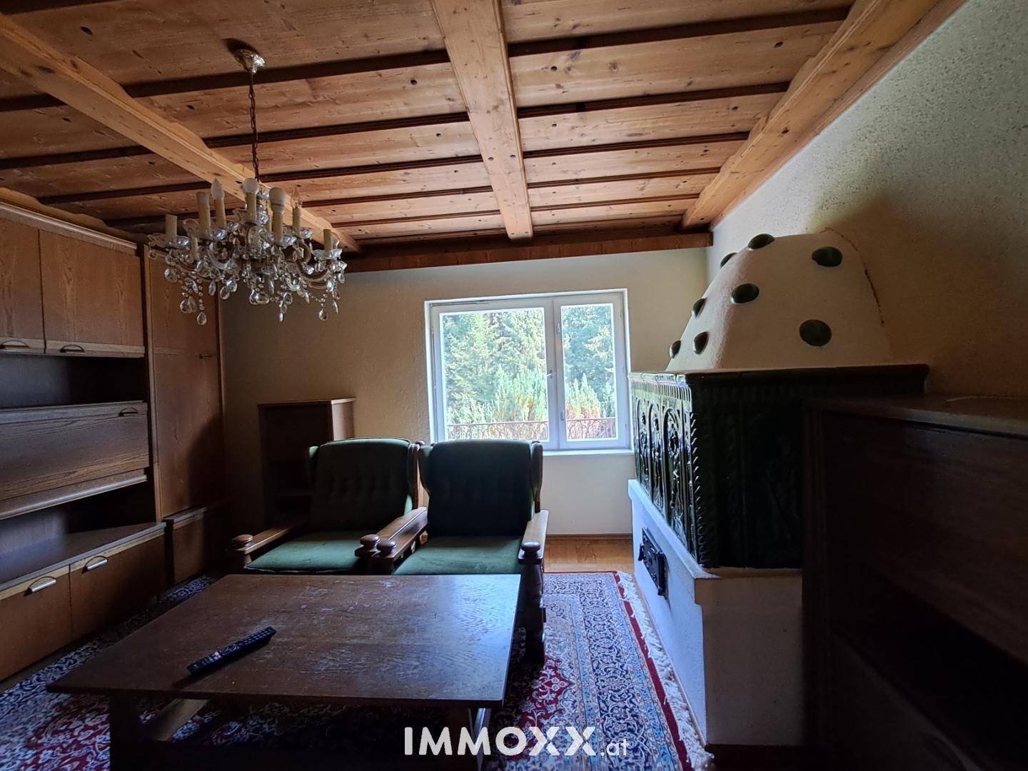Rustikales Wohnzimmer mit Holzbalkendecke, Kachelofen und Blick ins Grüne.