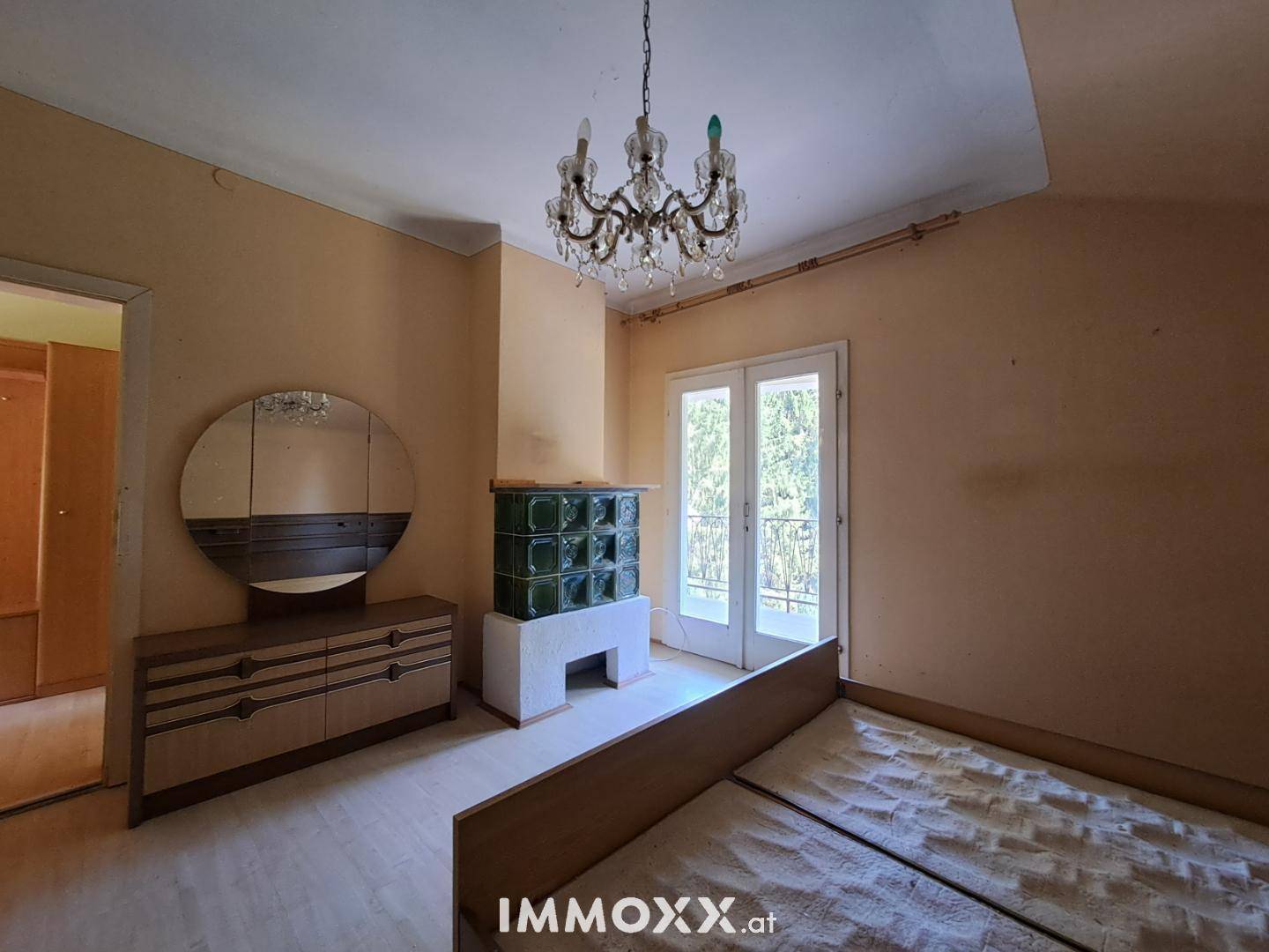 Schlafzimmer mit traditionellem Kachelofen, Kronleuchter und Zugang zum Balkon.