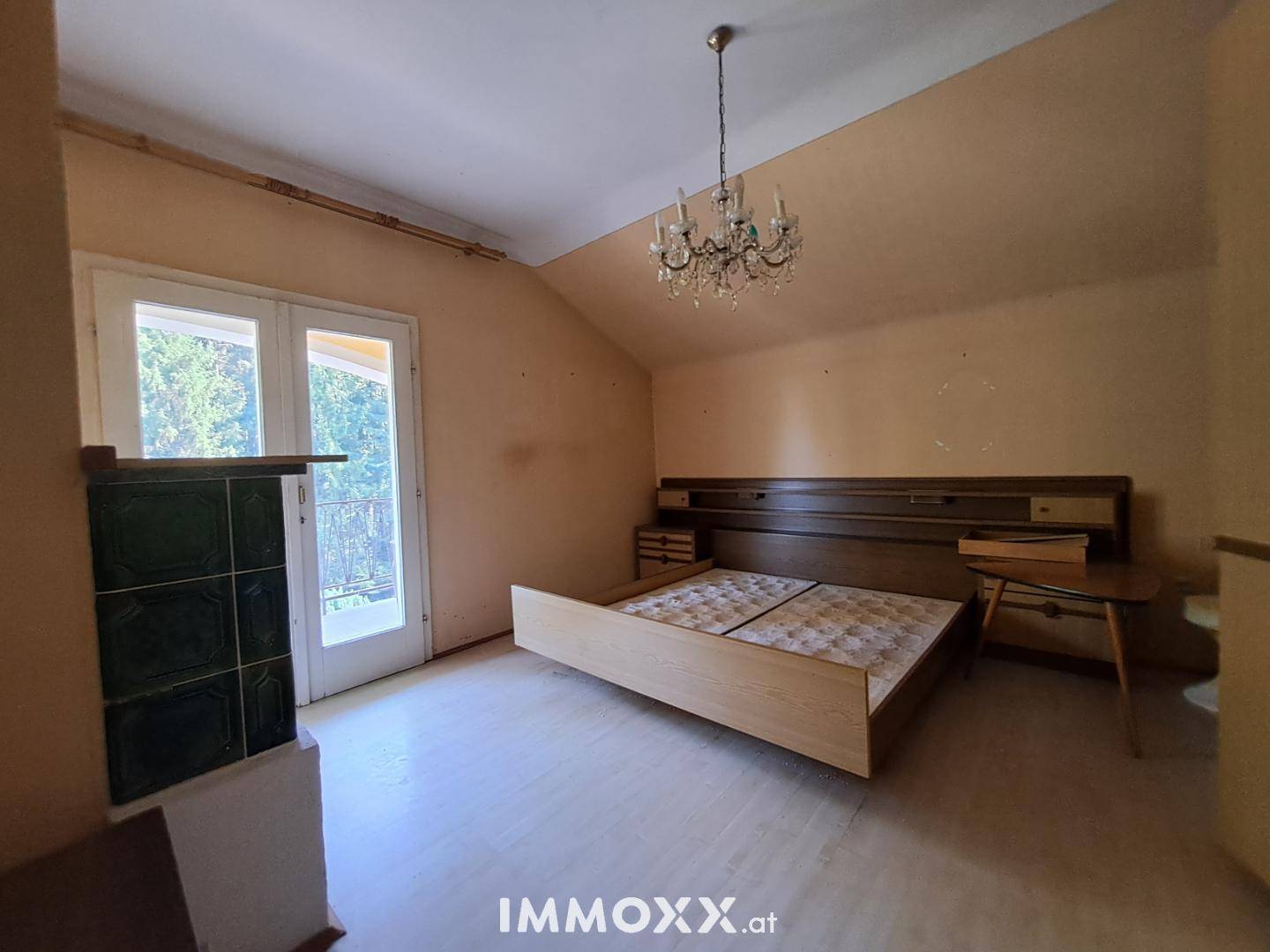 Schlafzimmer mit Kachelofen, Holzboden und Zugang zu einem französischen Balkon.